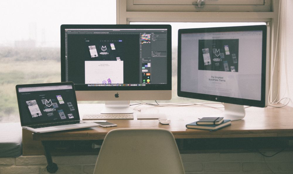 Web design workspace with a website displayed across a laptop and desktop monitors