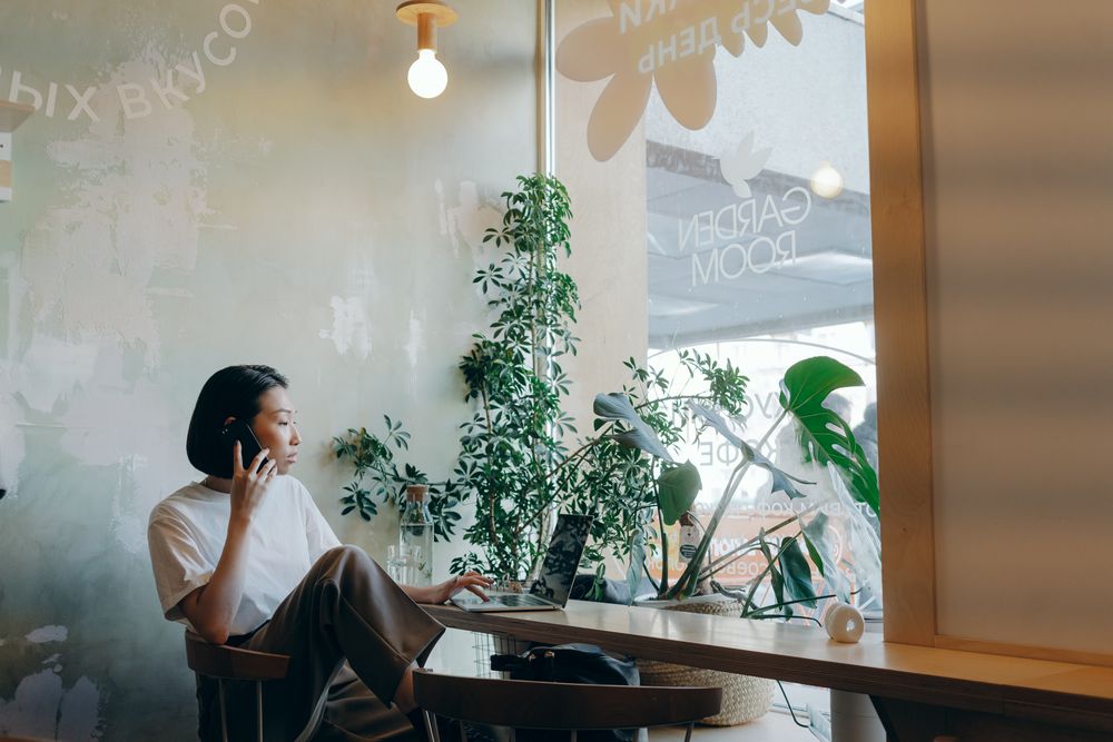 A woman using her phone and laptop at a café
