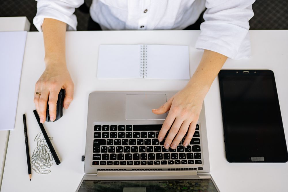 Person working at a laptop with a notebook and tablet on their desk